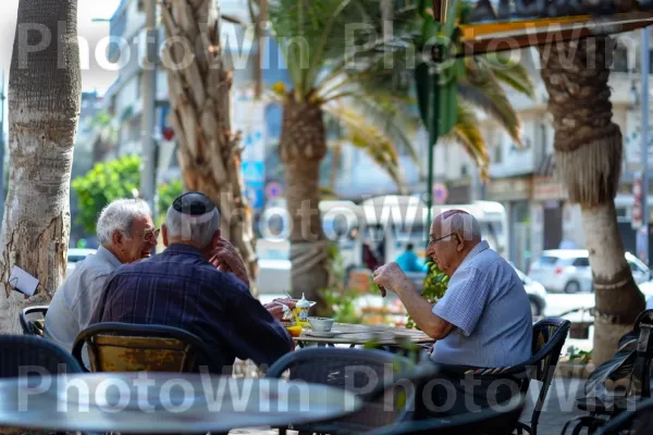 קשישים משוחחים בבית קפה בתל אביב, ממדינת ישראל. עֵץ, צהוב, שולחן חיצוני