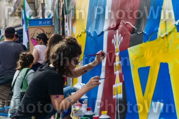 אמן רחוב מצייר ציור קיר תוסס בסמטה עירונית, ממדינת ישראל. חולצה קצרה, כֵּיף, אמן