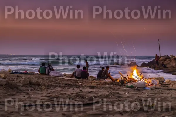 קבוצת חברים נהנית ממדורת חוף בשקיעה, ממדינת ישראל. ענן, עץ, צורות קרקע חופיות ואוקיאניות