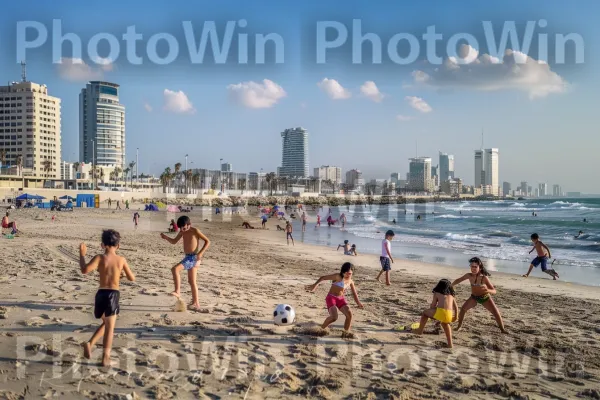 ילדים משחקים כדורגל בחוף הים בתל אביב, ממדינת ישראל. ענן, שְׁעוֹת הַיוֹם, אנשים על החוף