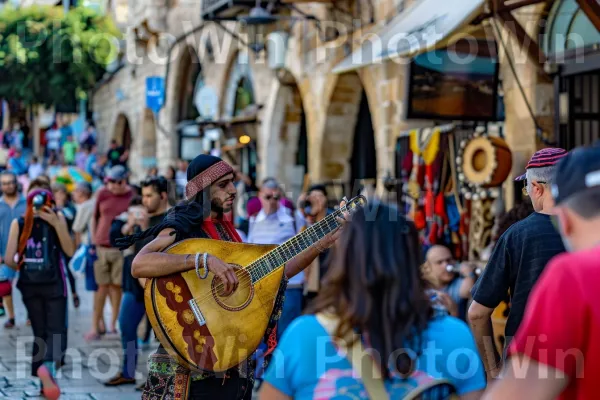 נגן רחוב משעשע תיירים ביפו, ממדינת ישראל. כלי נגינה, כובע, פְּנַאִי