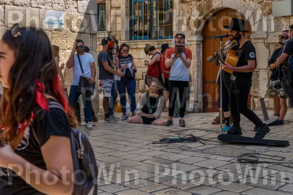 אמני רחוב משעשעים המונים בעיר העתיקה, ממדינת ישראל. מכנסיים, כלי נגינה, מרחב ציבורי