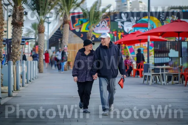 זוג מבוגרים מטייל בטיילת התוססת של תל אביב. צמח, כובע, פני הכביש