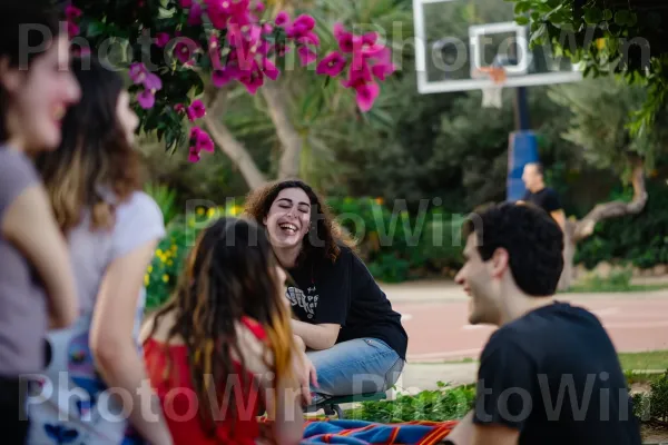 קבוצת חברים צוחקת ומפטפטת בפארק תל אביבי, ממדינת ישראל. צמח, תַצלוּם, דֶשֶׁא