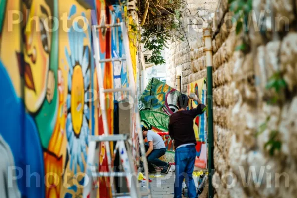 אמני רחוב מציירים ציורי קיר בסמטאות צפת, ממדינת ישראל. צֶבַע, צהוב, גרפיטי