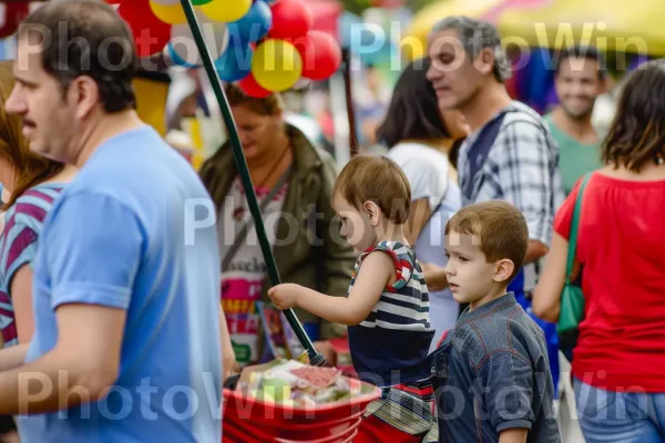 משפחות חוקרות בשמחה יריד רחוב חגיגי, מלא באוכל ובידור. שְׁעוֹת הַיוֹם, חולצה קצרה, צהוב